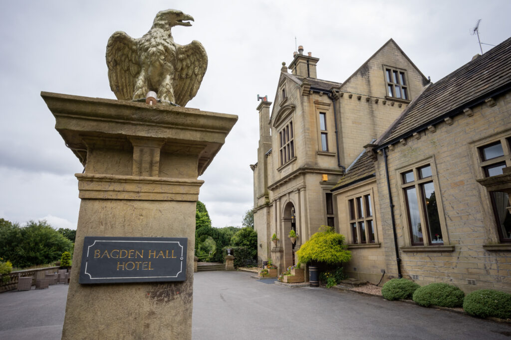 Stone eagle statue and sign reading "Bagden Hall Hotel" at the entrance of a large, historic stone building with tall windows and landscaped greenery. Focus Photography by Tim Teasdale