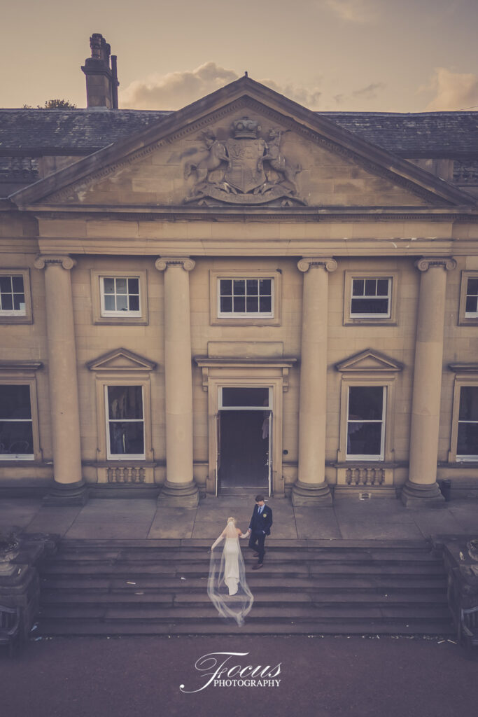 Bride and groom stand on steps outside a grand neoclassical building with columns and ornate carvings at sunset