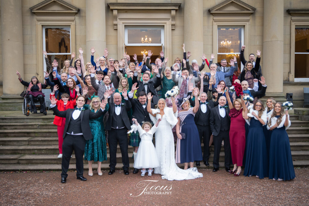 Large wedding group celebrating outside elegant building.