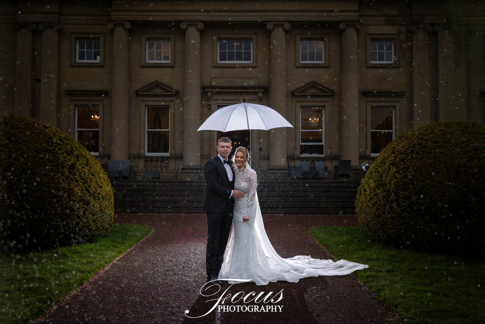Bride and groom under umbrella outside grand manor