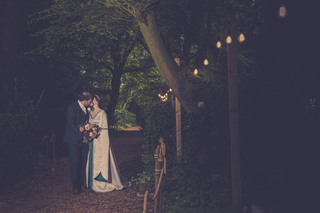 Bride and groom kissing under woodland lights
